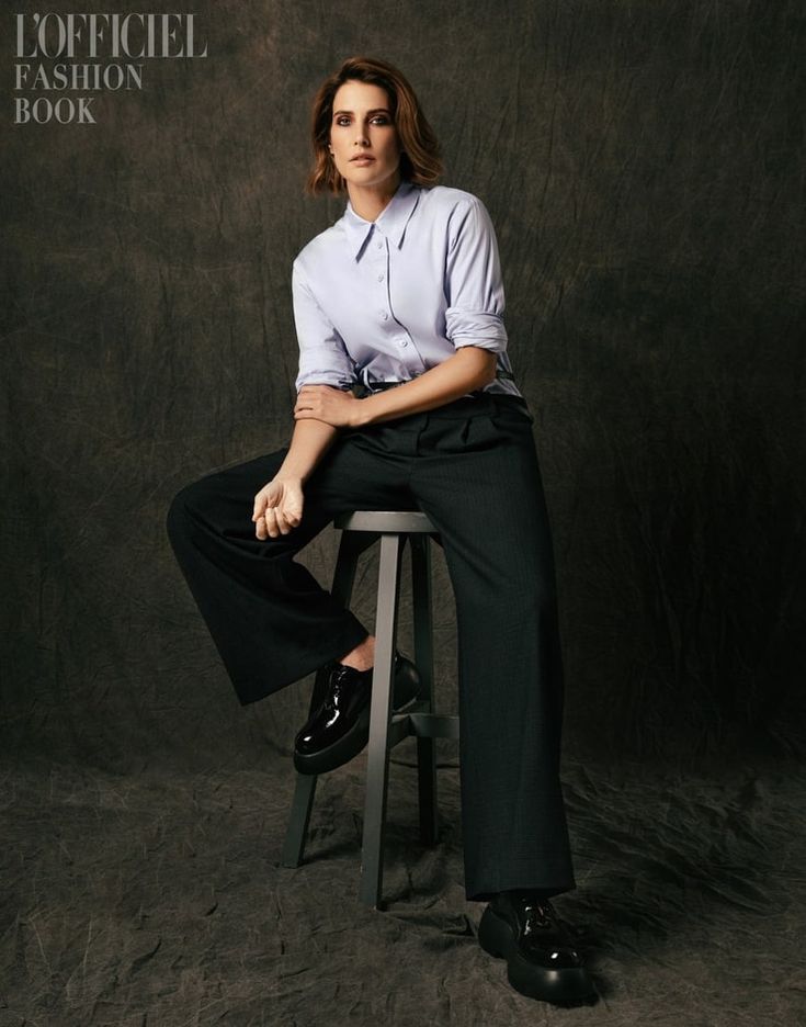 a woman sitting on top of a stool in front of a black background with her legs crossed