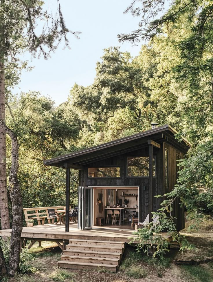 a small cabin in the woods with stairs leading up to it's patio area