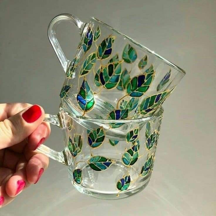 a hand holding a glass tea cup with green leaves on the bottom and gold trimmings