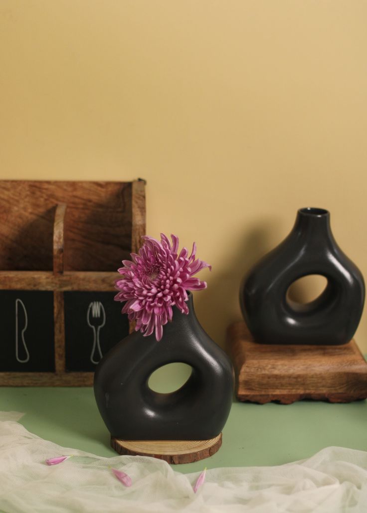 two black vases with pink flowers in them on a green tablecloth next to a wooden crate