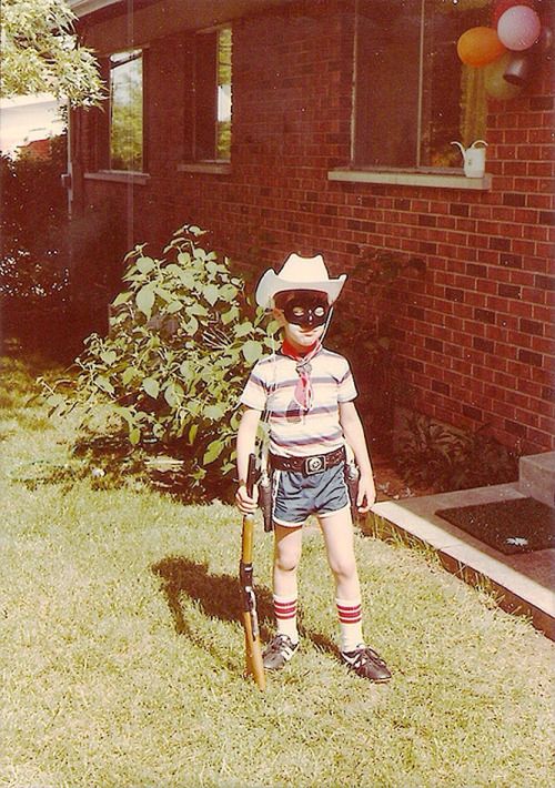 a young boy wearing a cowboy hat and holding a baseball bat in front of a house