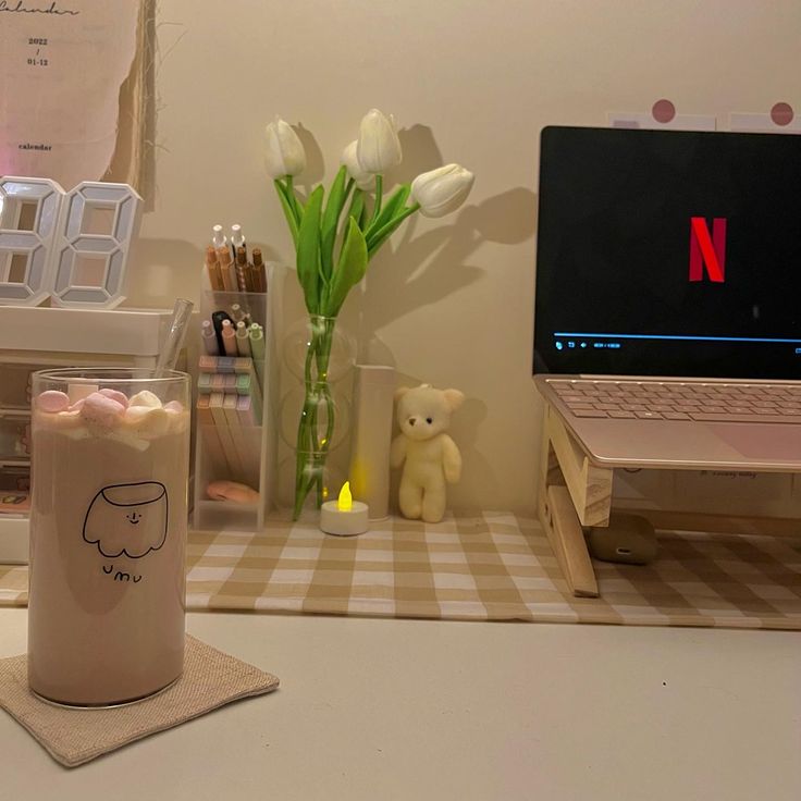 a laptop computer sitting on top of a desk next to a vase filled with flowers