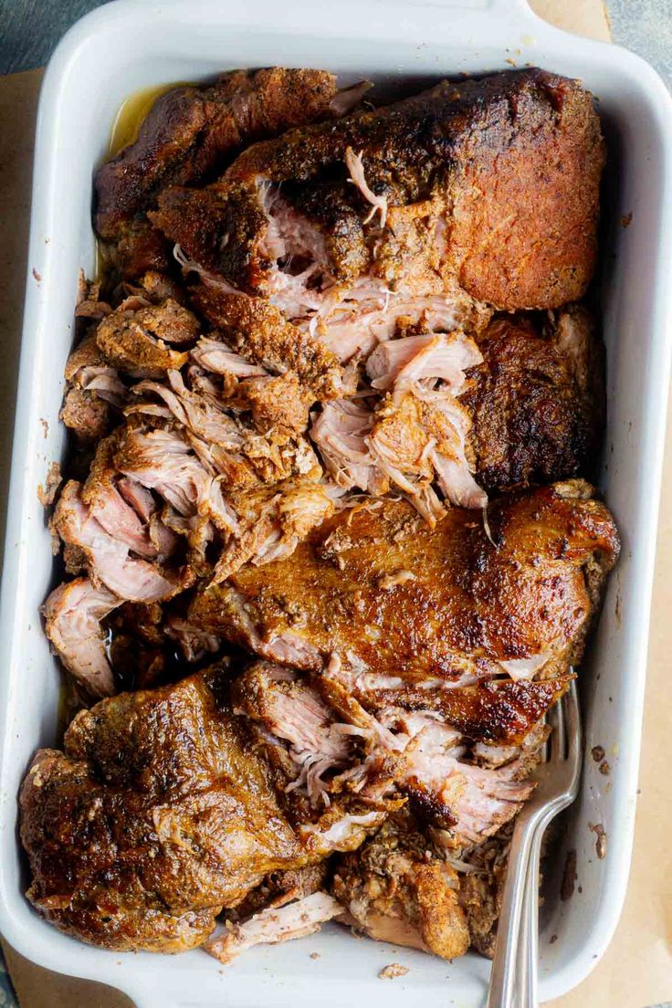 meat in a white casserole dish with a fork and spoon next to it