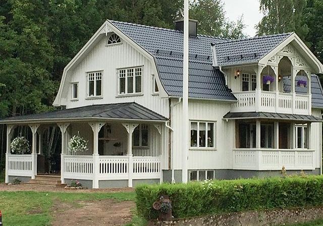 a large white house sitting in the middle of a lush green field next to a forest