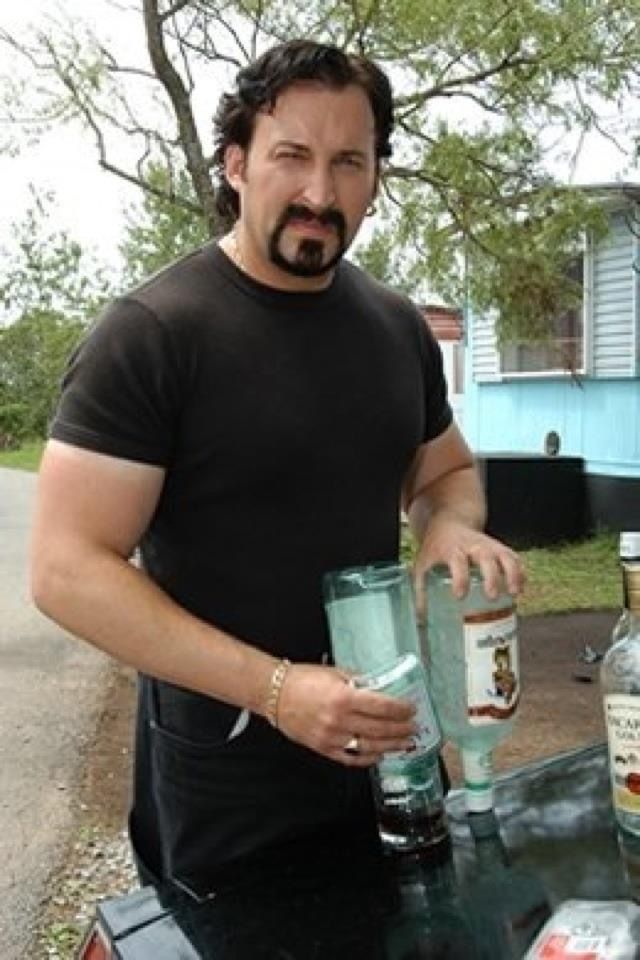 a man standing next to a table with bottles on it and a glass in front of him