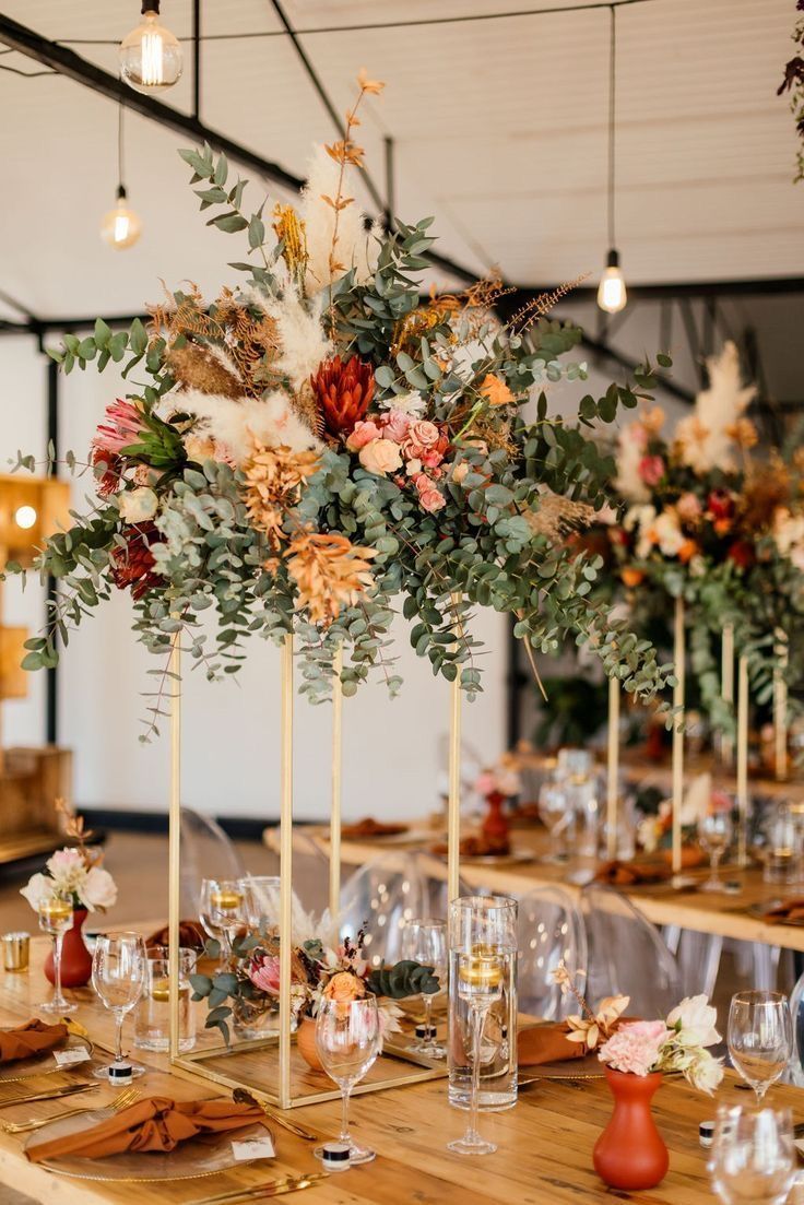 an arrangement of flowers and greenery is displayed in tall vases on the table