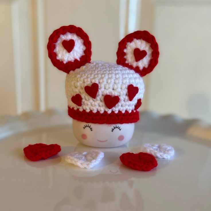 a crocheted hat with ears and hearts on it sitting on a white table