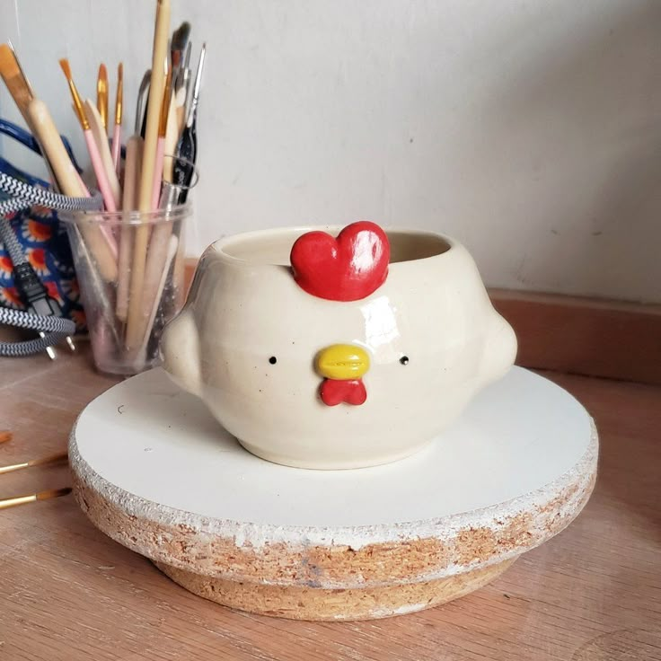 there is a ceramic chicken cup on the counter next to some pencils and markers