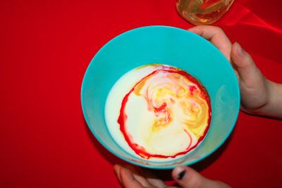 two hands holding a blue bowl with white and red liquid in it on a red table