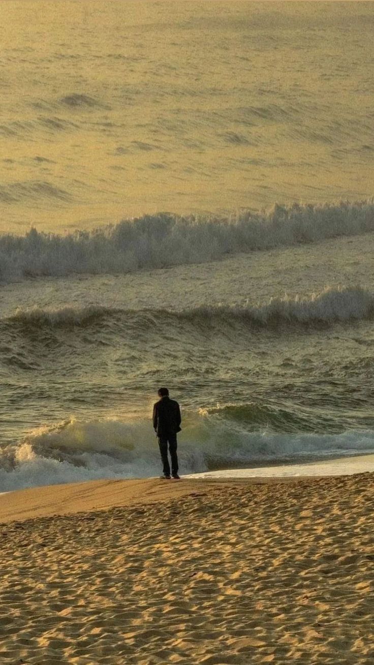 a man standing on top of a sandy beach next to the ocean