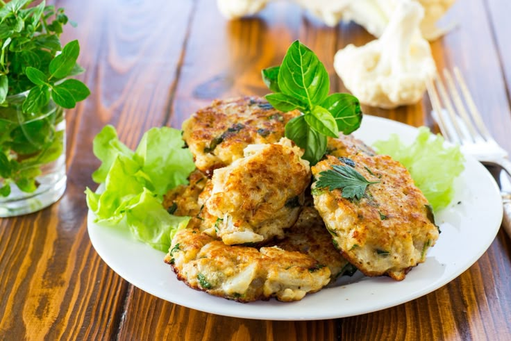 crab cakes with lettuce on a plate next to a fork and glass of water