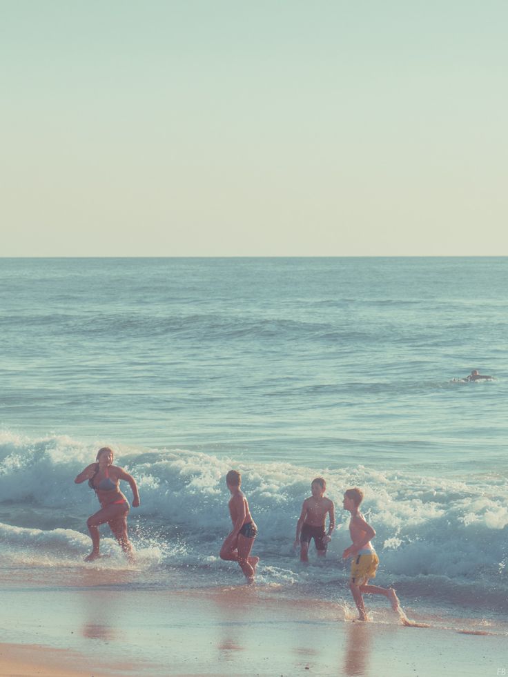 several people are running on the beach in front of the ocean and one person is swimming