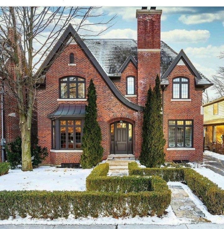 a large brick house with hedges and trees in the front yard on a snowy day