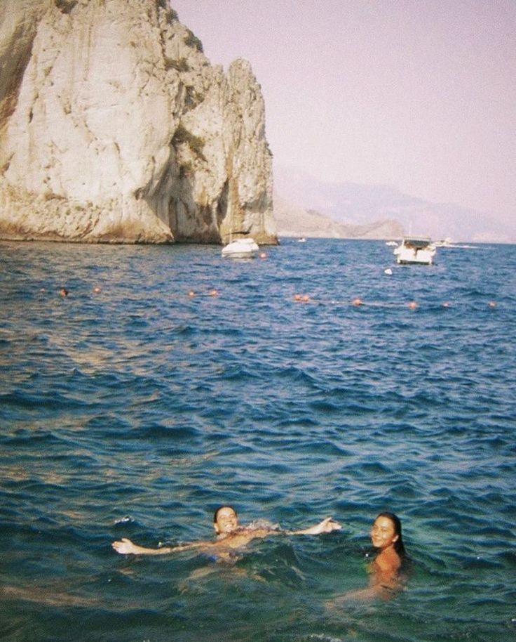 two people swimming in the ocean next to large rocks