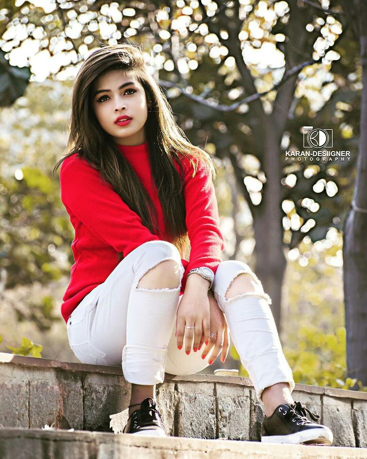 a young woman sitting on top of a brick wall next to a tree and looking at the camera