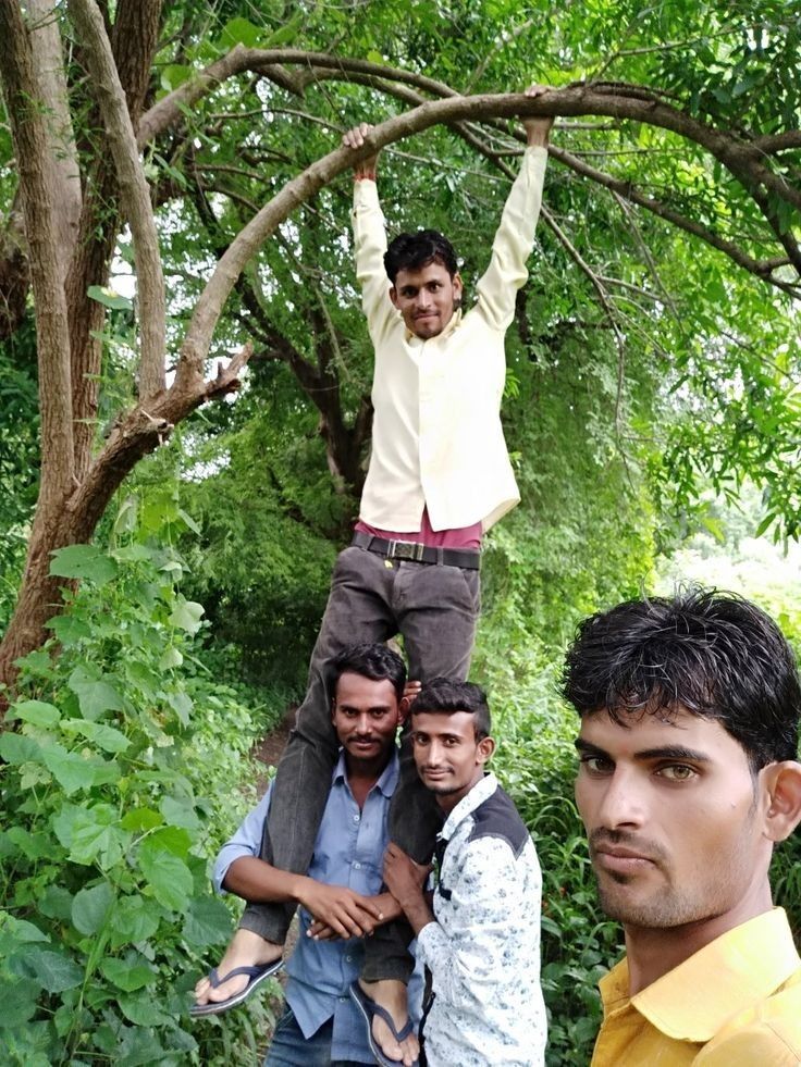 three men standing on top of each other in front of some trees and bushes with one man holding his arms up