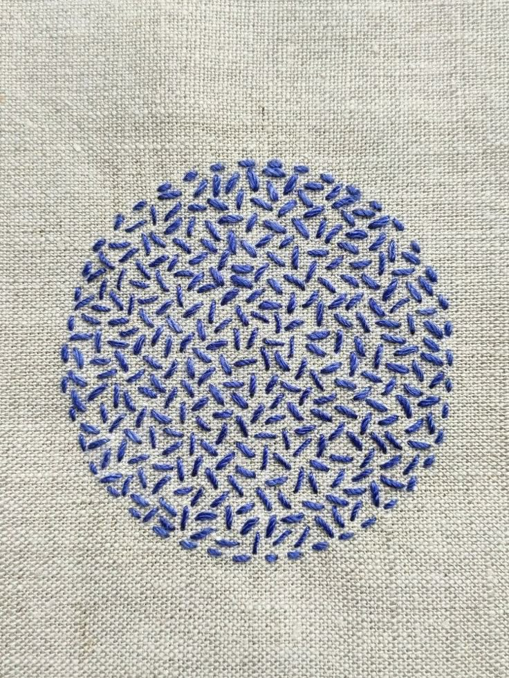 a blue and white circular design on a piece of linen with stitches in the middle