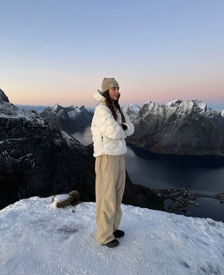 a woman standing on top of a snow covered mountain next to a body of water