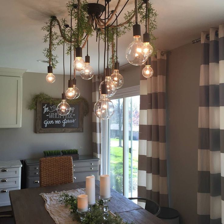 a dining room table with candles on it and hanging lights above the table in front of a sliding glass door