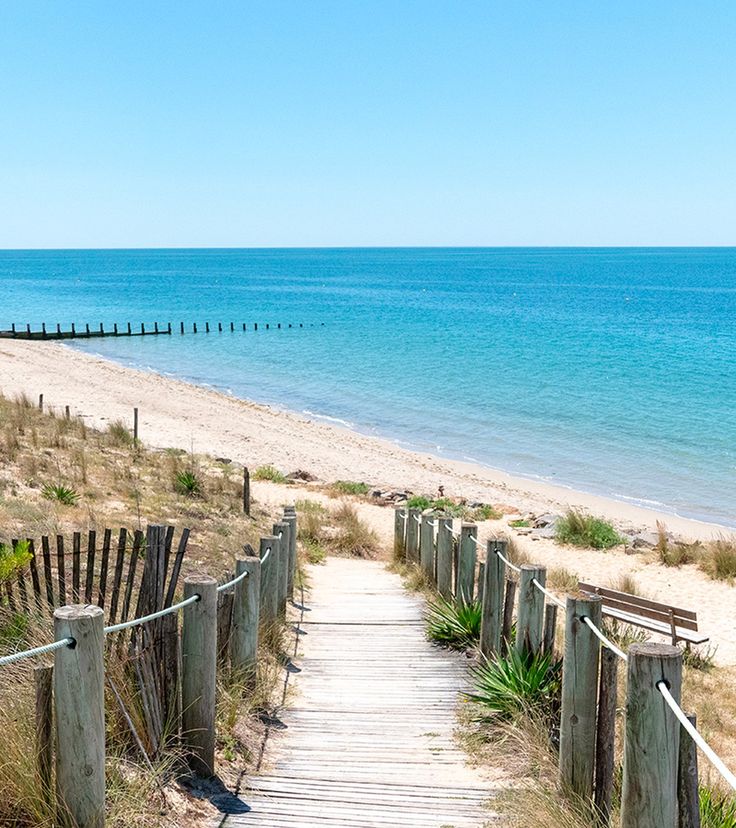 a wooden walkway leading to the beach with blue water in the backgrounnd