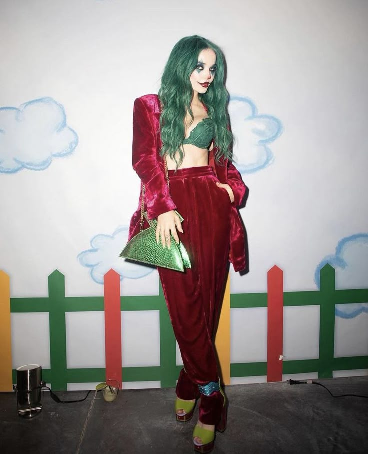 a woman with green hair wearing a red outfit and holding a purse in front of a wall