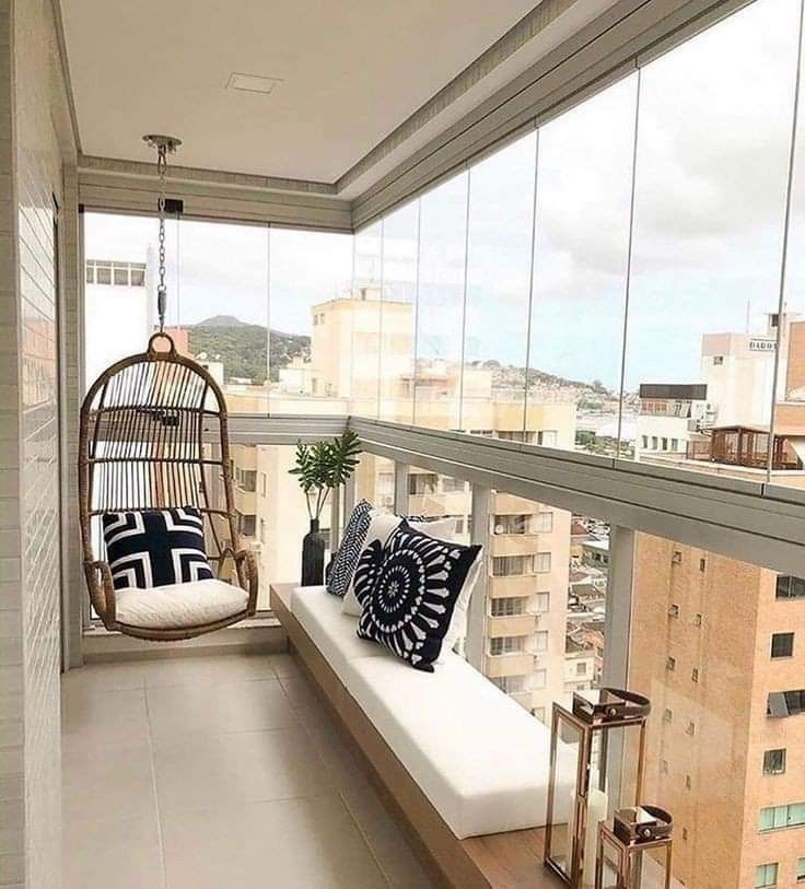 a balcony with a swing chair and pillows on the floor next to a large window