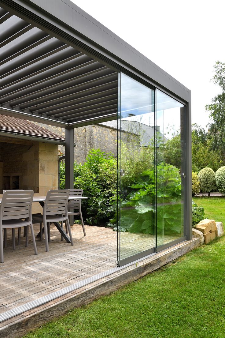 an outdoor dining area with glass walls and patio furniture on the outside, surrounded by lush green grass