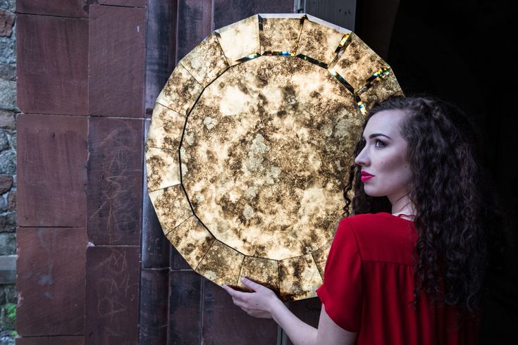 a woman holding up a large piece of art that looks like a sundial on a brick wall