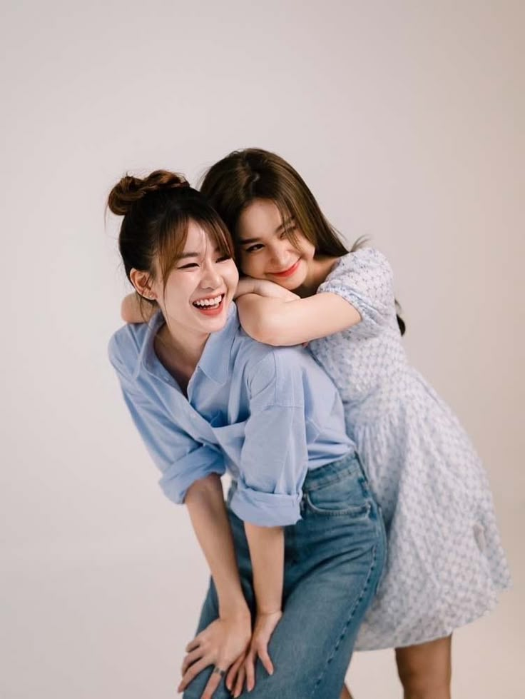 two young women hugging each other while posing for the camera in front of a white background