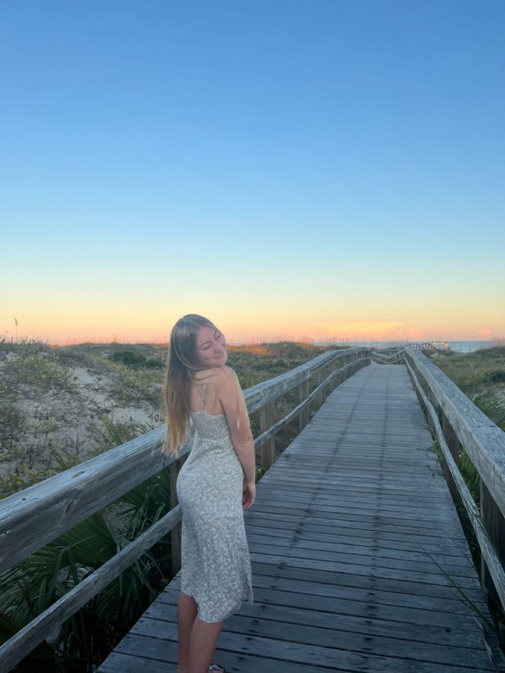 a woman standing on a boardwalk at the beach looking up into the sky with her eyes closed