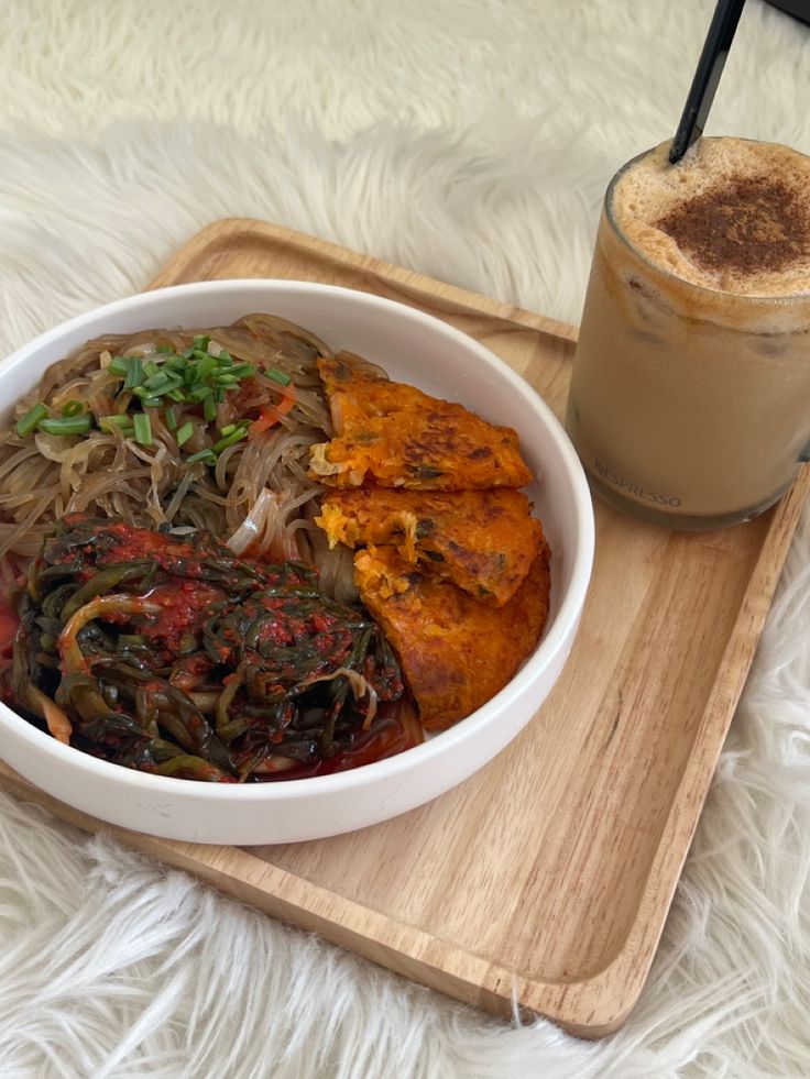 a white bowl filled with food next to a cup of coffee on a wooden tray