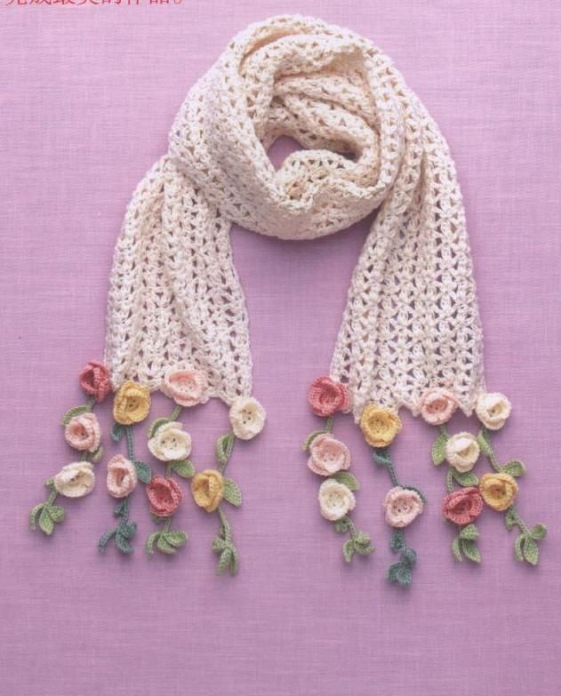 a white scarf with crochet flowers hanging from it's sides on a pink background