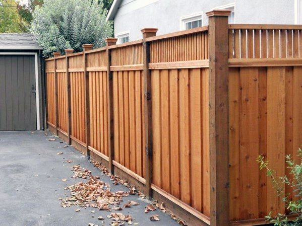 a wooden fence in front of a house with leaves on the ground next to it