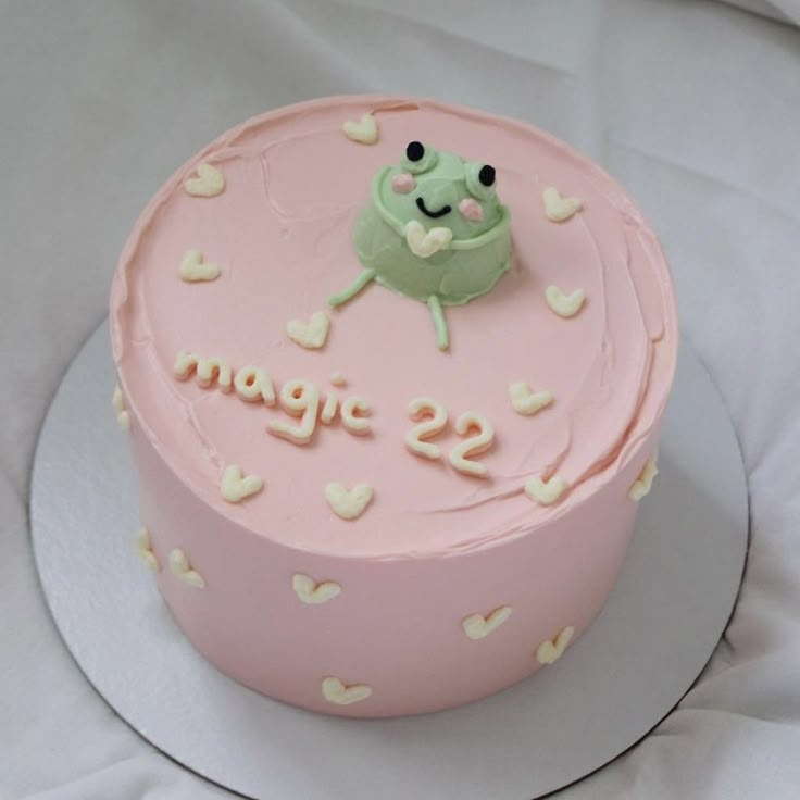 a pink cake with white hearts and a green frog on top that says s'more