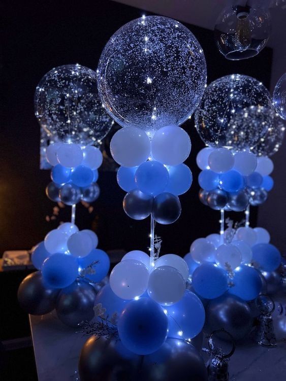 blue and white balloons are hanging from the ceiling in front of a black tablecloth