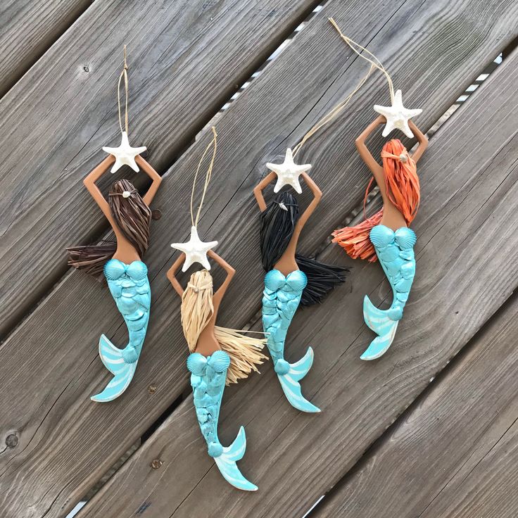 three little mermaid ornaments hanging on a wooden fence with starfish and seashells