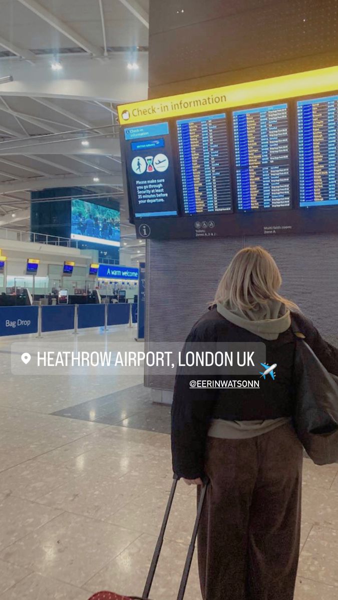 a woman is pulling her luggage through an airport with the check in information board behind her