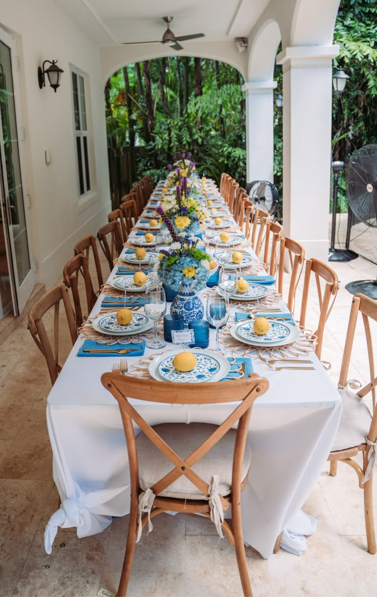 a long table set up with blue and white plates on it for an outdoor dinner