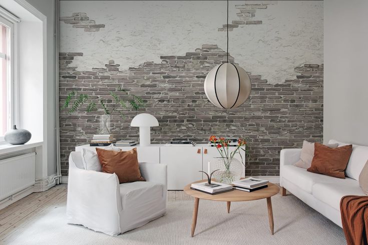 a living room with two white couches and a table in front of a brick wall