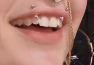 a woman with piercings on her nose and teeth is smiling at the camera while wearing an ear chain