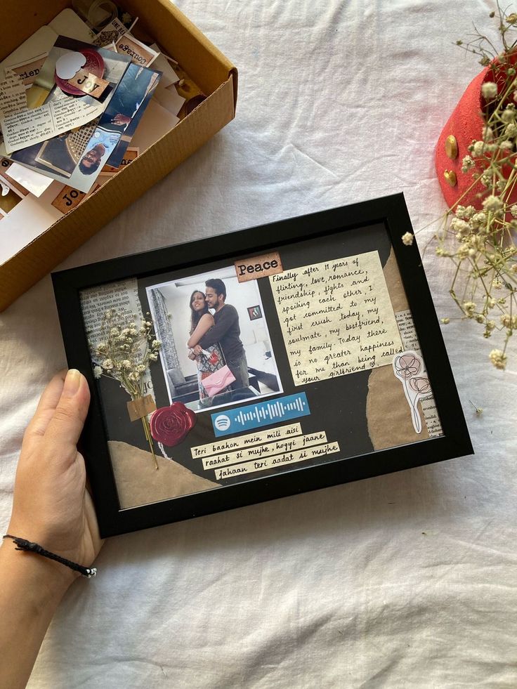 a person holding up a framed photo in front of a box with pictures on it