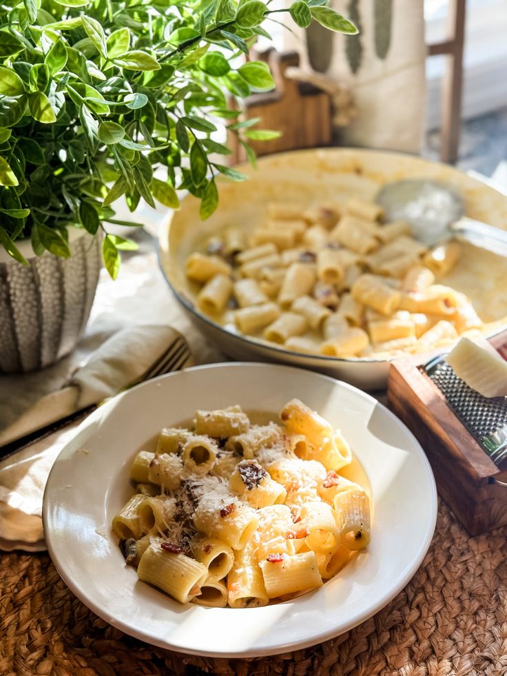 a plate of pasta with cheese and sauce next to a potted plant on a table