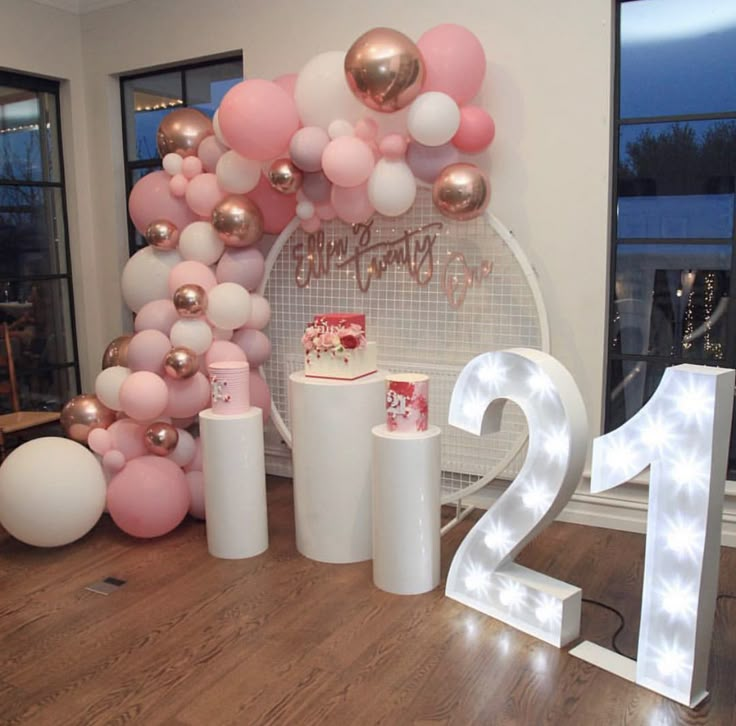 a table topped with lots of balloons next to a number twenty sign and two cakes