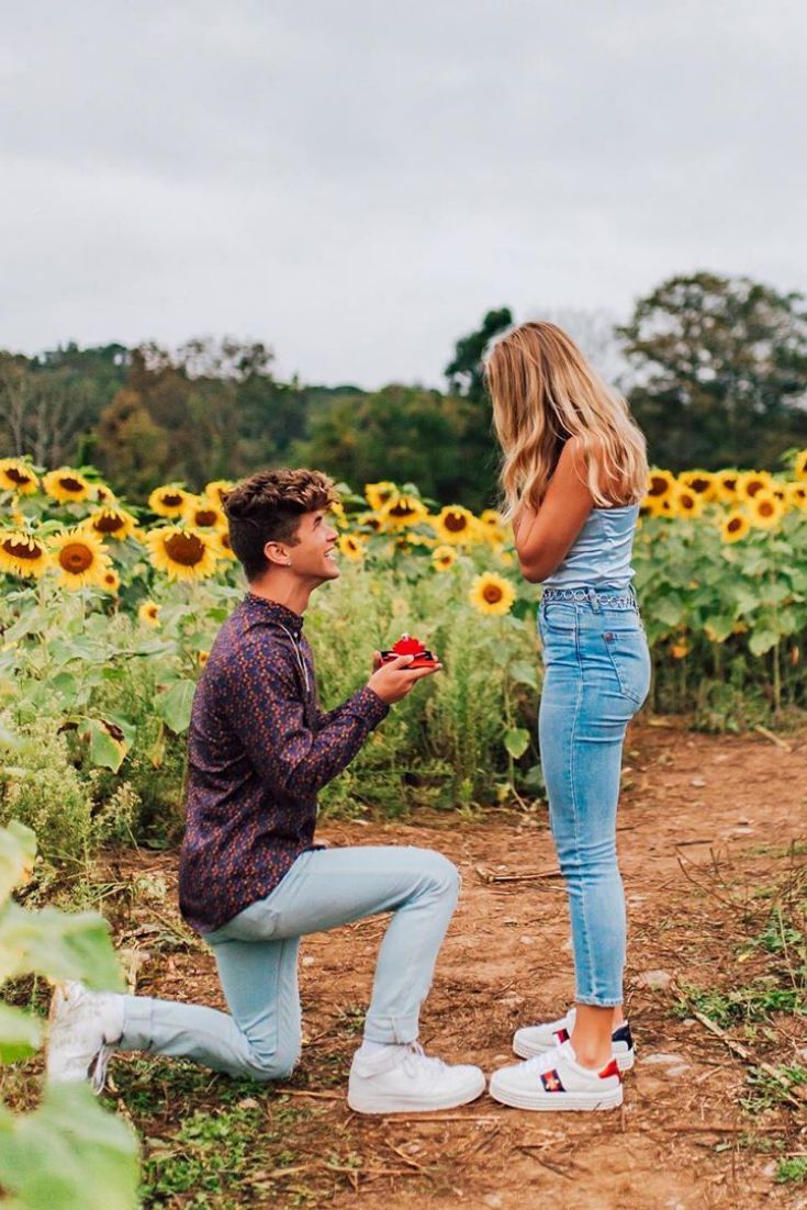 a man kneeling down next to a woman in a field full of sunflowers