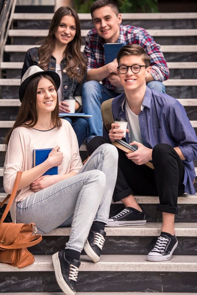 group of students sitting on steps with notebooks and books in hand smiling at the camera