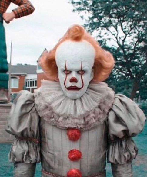 a creepy clown is standing in front of a man with an orange hair and white face