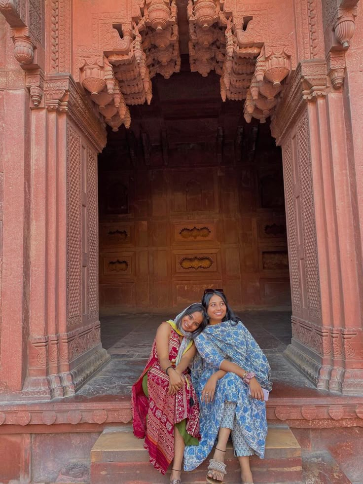 two women sitting on steps in front of an ornate building with carved pillars and doorways