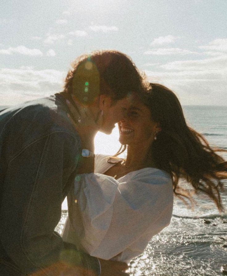 a man and woman kissing on the beach with sun shining in the water behind them