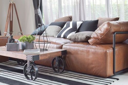 a brown leather couch sitting in a living room next to a wooden table and chair