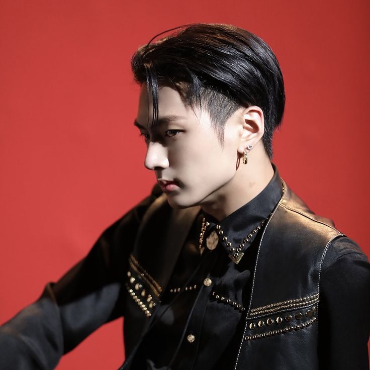 a young man with black hair and piercings sitting on a chair in front of a red wall